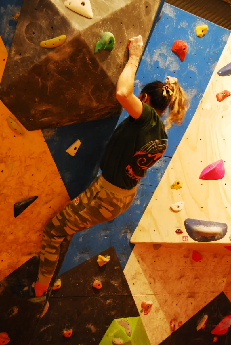 Escaladora con polera negra y pantalón camuflado en un desplome amarillo y azul
