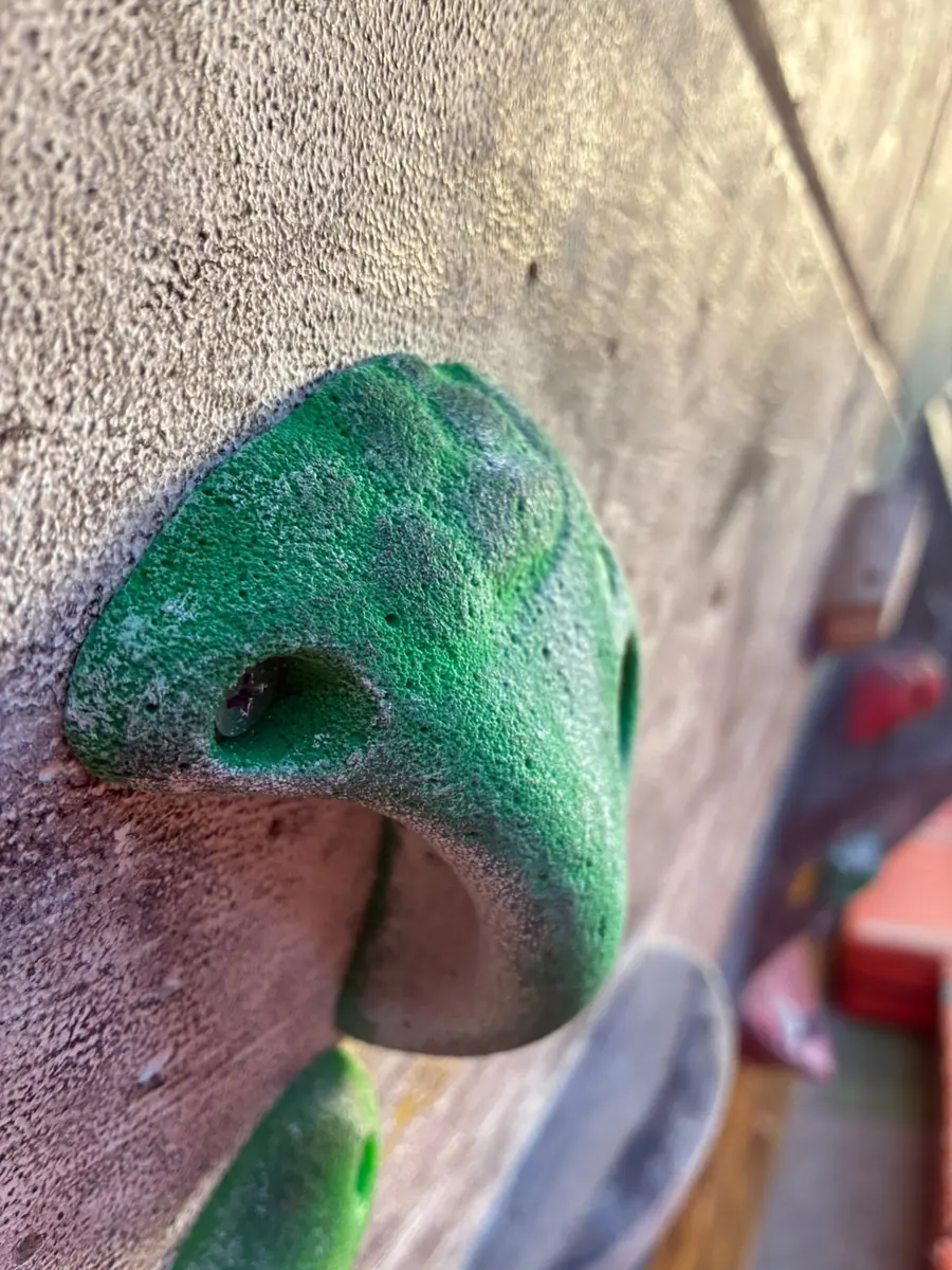 Una presa verde con magnesio, atornillada a un panel de textura rugosa, vista de muy cerca